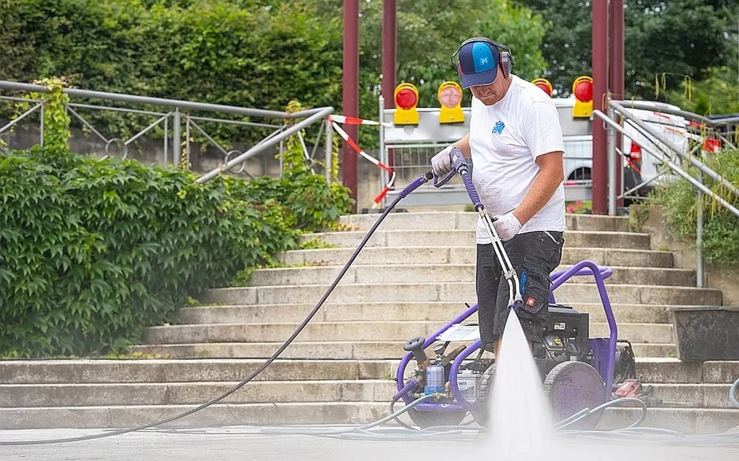 Marlett GbR – Reinigungs- & Sanierungstechnik – eine Person, die einen Hochdruckreiniger verwendet, um eine Betonoberfläche im Freien, wahrscheinlich einen Weg oder eine Treppe, zu reinigen.